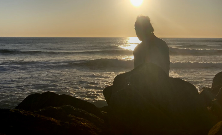 Uri Frazier sitting on rocks in front of a Pacific Ocean sunset.