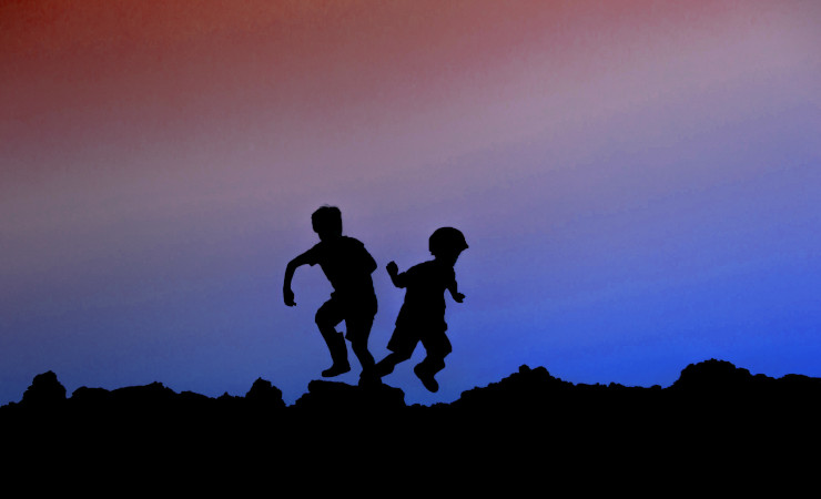 The silhouette of two kids running in opposite directions across a rocky terrain.